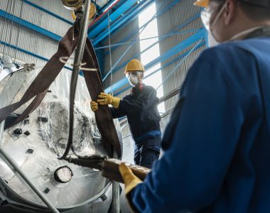 Low-angle view of two workers handling equipment for lifting industrial steam boilers